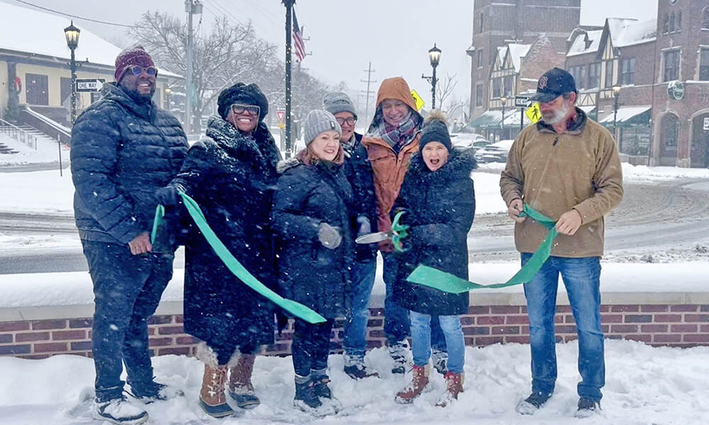 Flossmoor Mayor Michelle Nelson holds up a giant pair of scissors and cuts the green ribbon with other Flossmoor village officials, marking the completion of the Downtown Flossmoor Streetscape Project. (Nick Ulanowski / H-F Chronicle)