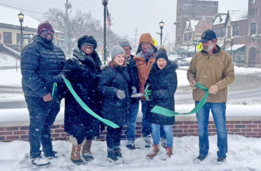 Flossmoor Mayor Michelle Nelson holds up a giant pair of scissors and cuts the green ribbon with other Flossmoor village officials, marking the completion of the Downtown Flossmoor Streetscape Project. (Nick Ulanowski / H-F Chronicle)