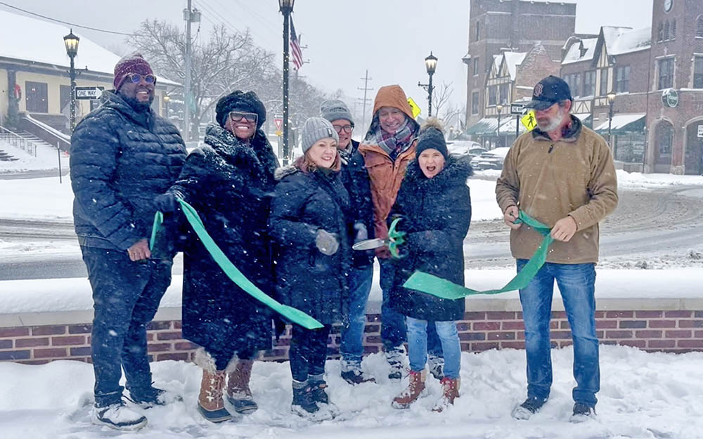 Flossmoor Mayor Michelle Nelson holds up a giant pair of scissors and cuts the green ribbon with other Flossmoor village officials, marking the completion of the Downtown Flossmoor Streetscape Project. (Nick Ulanowski / H-F Chronicle)