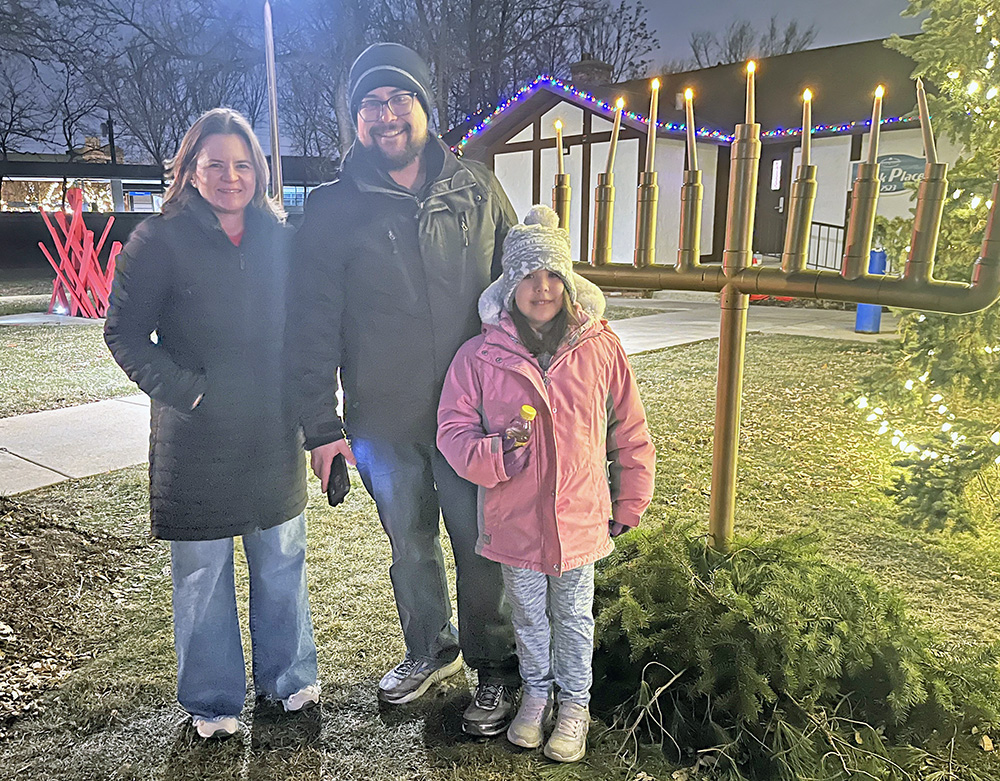 Flossmoor Mayor Michelle Nelson, left, Flossmoor resident Jacob Schoeneman, center, and his 7-year-old daughter, Holly Schoeneman, in front of the Flossmoor Park menorah. (Nick Ulanowski / H-F Chronicle)