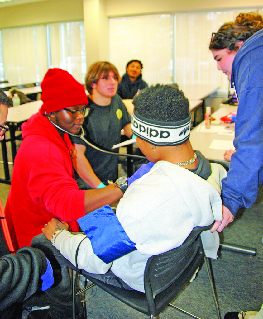 Evaluator Laila Judah (standing) watches as student Ethan Randle listens to a patient's heart during a practicum lesson at PSC's EMT training. (Provided photo)