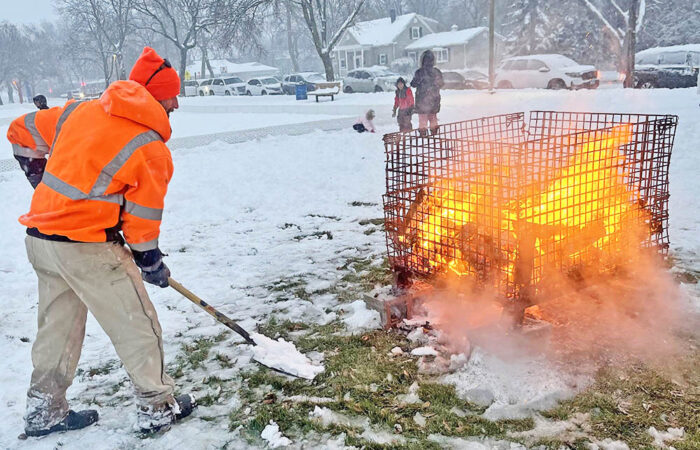 Gabe Gacsko, a maintenance worker with the Homewood-Flossmoor Park District, shovels snow into the area under the bonfire. (Nick Ulanowski / H-F Chronicle)