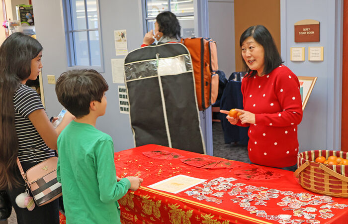Molly Deugaw explains the meaning behind Lunar New Year treats and traditions as children gather around the food table at Flossmoor Public Library. (Nuha Abdessalam/H-F Chronicle)