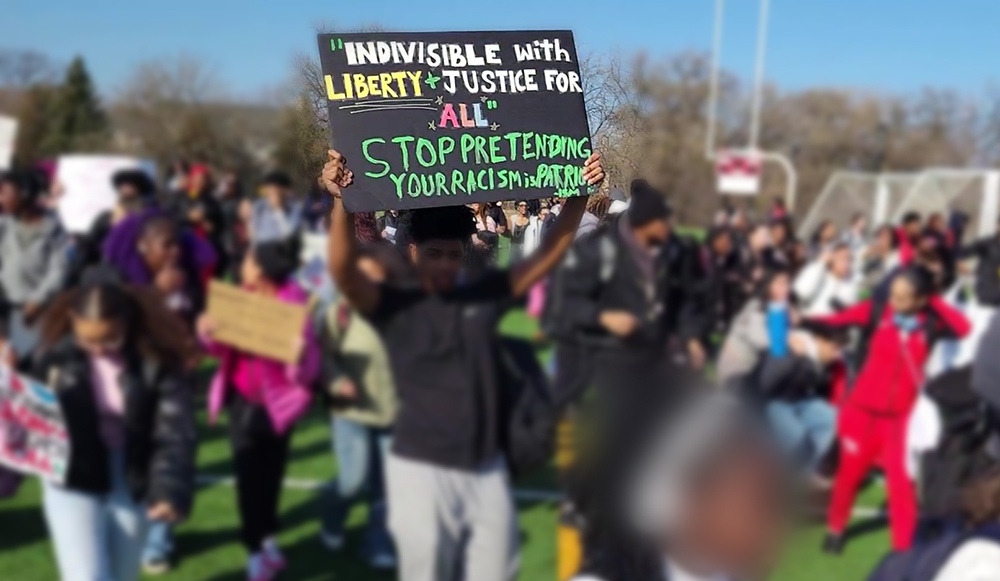 An H-F High student holds up a sign that reads "'Indivisible with liberty + justice for all.' Stop pretending your racism is patriotism." Students demonstrated Friday, Feb. 13, in protest of federal immigration enforcement tactics. (Eric Crump/H-F Chronicle)