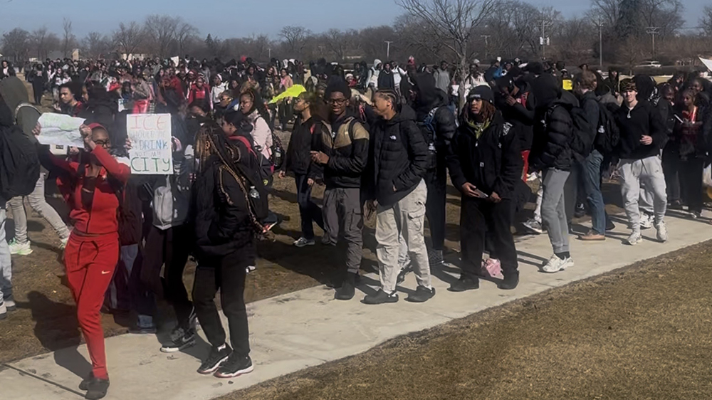 A Homewood-Flossmoor High School student with a sign that says "ICE should be in my drink, not my city" and other students marching on campus near Flossmoor Road. (Nick Ulanowski/H-F Chronicle)