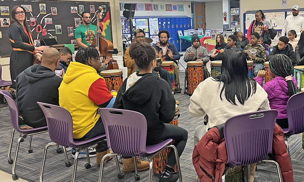 Teacher Jon Pettis, in the tan jacket, leads the drum circle at the Churchill School Black History month event on Feb. 26. Orchestra teacher Bryson Robinson-Levant and Churchill Elementary parent Laura Miller play instruments behind him. (Nick Ulanowski H-F Chronicle)