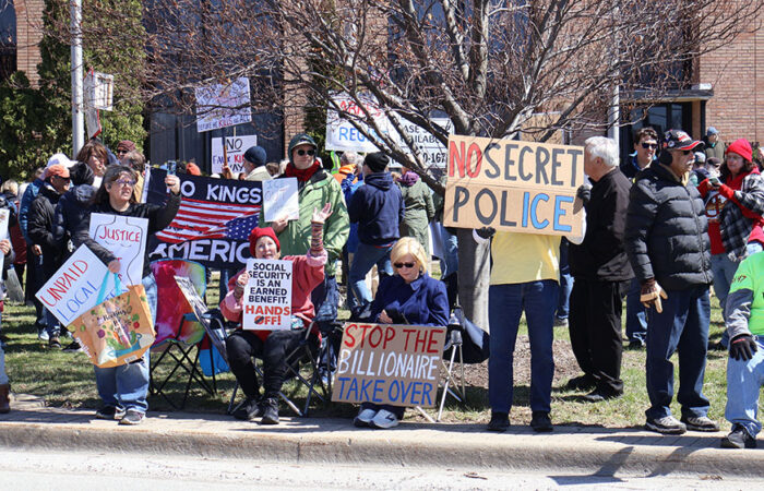 A packed stretch of lawn and sidewalk fills with people holding signs and waving toward passing cars during Saturday’s rally in Homewood. (Nuha Abdessalam/H-F Chronicle)