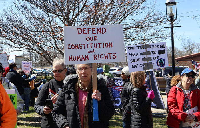 A protester holds a “Defend Our Constitution and Human Rights” sign as the crowd fills in around the Homewood Veterans Memorial. (Nuha Abdessalam/H-F Chronicle)