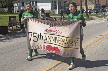 Two softball players carry a banner in the opening day parade recognizing Homewood Baseball and Softball's 75th anniversary. (Nick Ulanowski / H-F Chronicle)