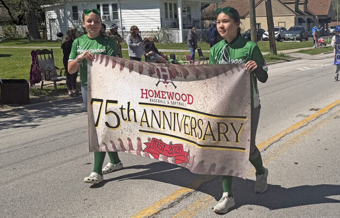 Two softball players carry a banner in the opening day parade recognizing Homewood Baseball and Softball's 75th anniversary. (Nick Ulanowski / H-F Chronicle)