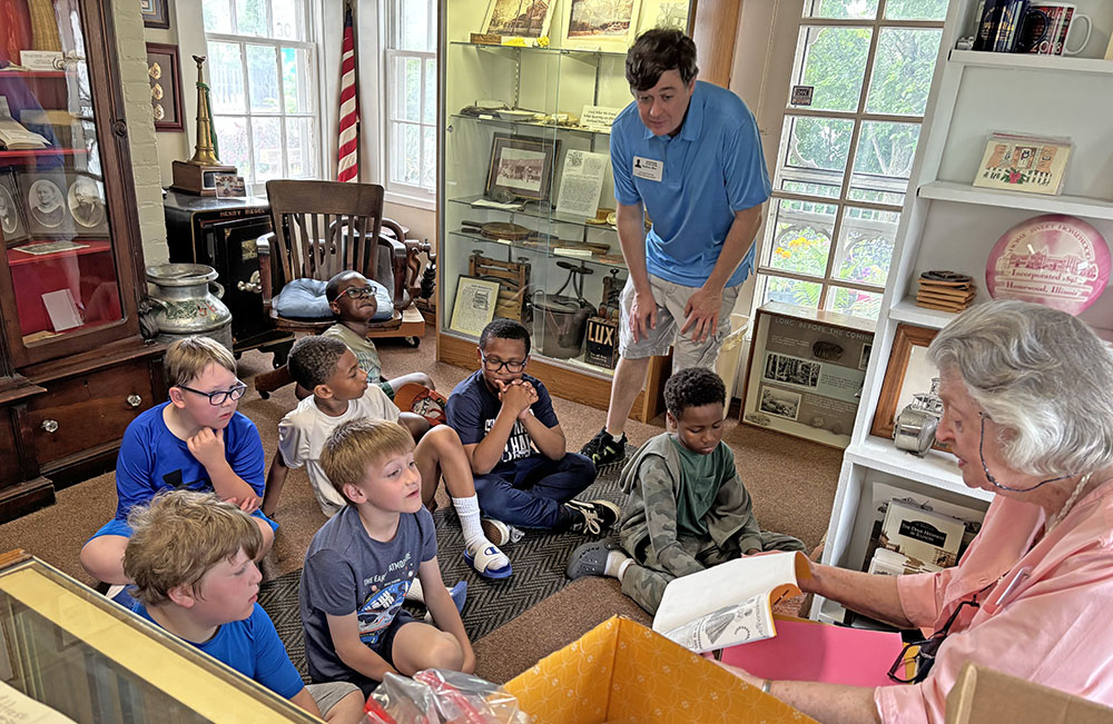 Elaine Egdorf, seated at right, shares local history with second graders during their field trip to the Homewood Historical Society. (Marilyn Thomas/H-F Chronicle)