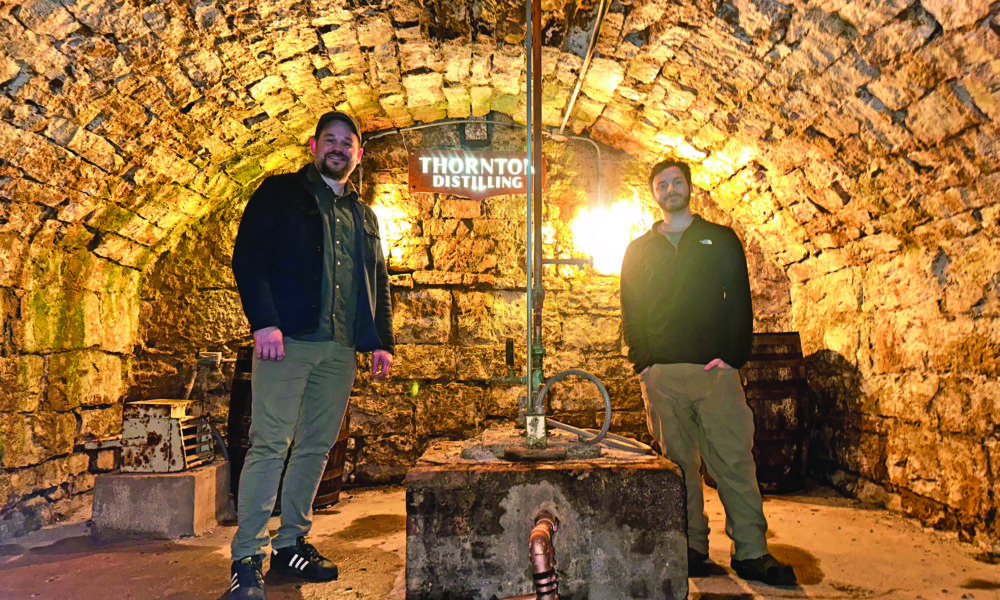Thornton Distilling owner Andrew Howell, left, and head distiller Ari Klafter stand beside the well that takes water directly from the spring underneath the building. (Provided photo)