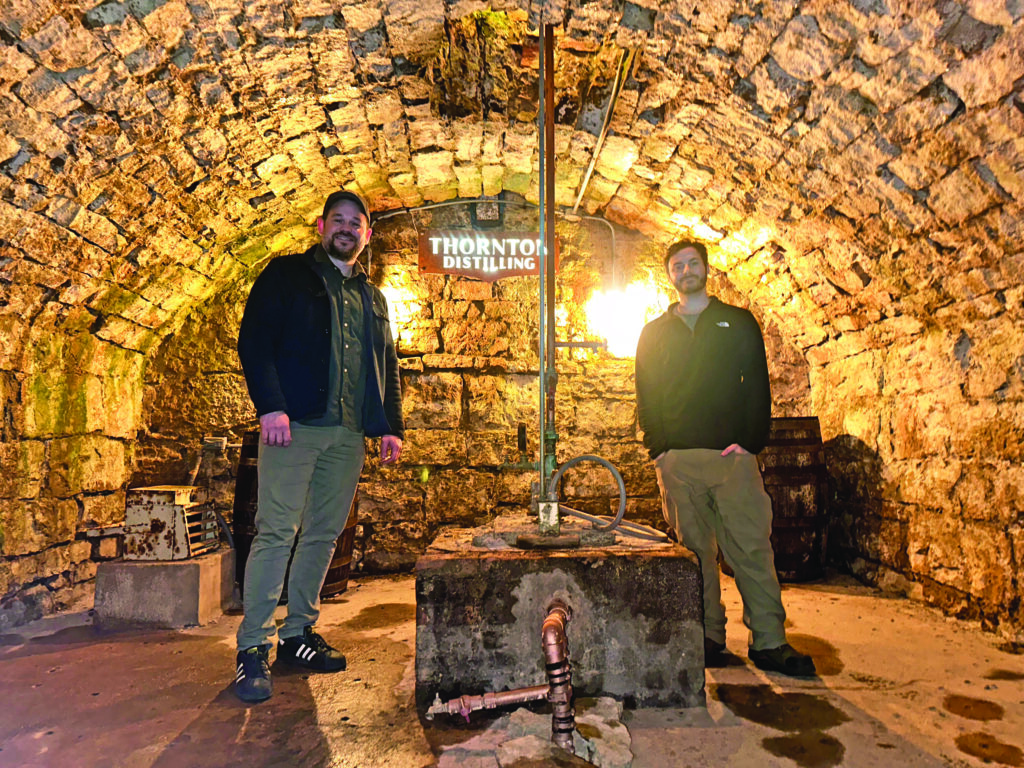 Thornton Distilling owner Andrew Howell, left, and head distiller Ari Klafter stand beside the well that takes water directly from the spring underneath the building. (Provided photo)